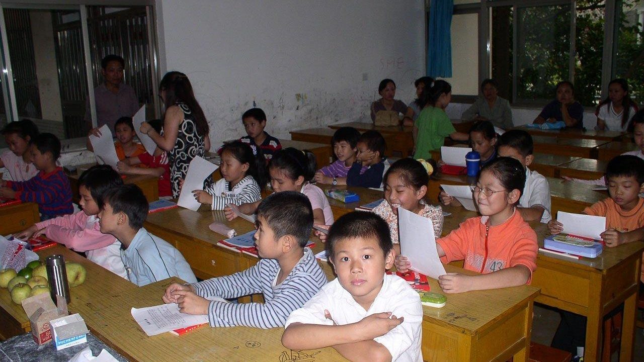 Empty elementary school classroom with small desks arranged in rows.