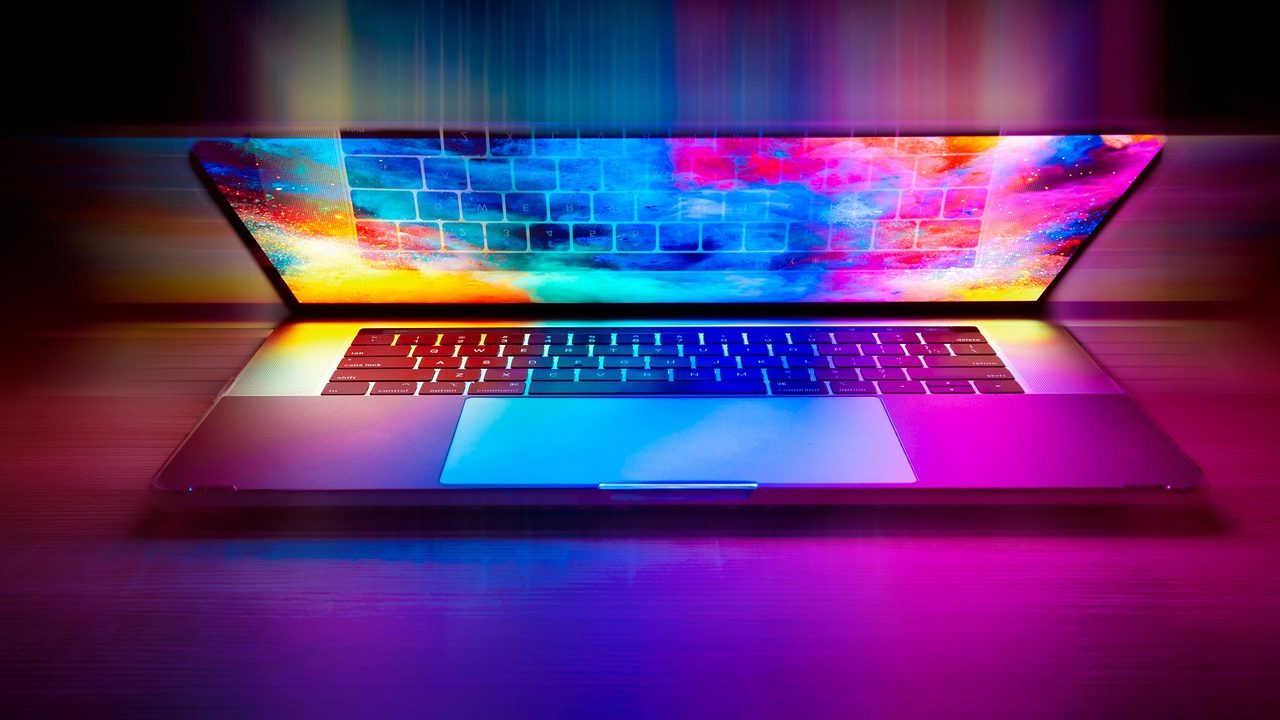 An open laptop sits on a wooden desk in warm morning light.