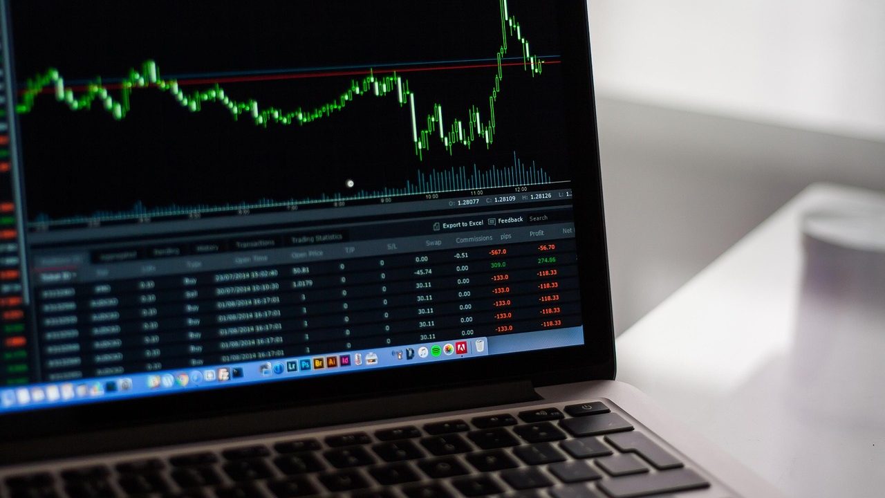 Multiple computer monitors displaying financial charts and data dashboards in an open office.