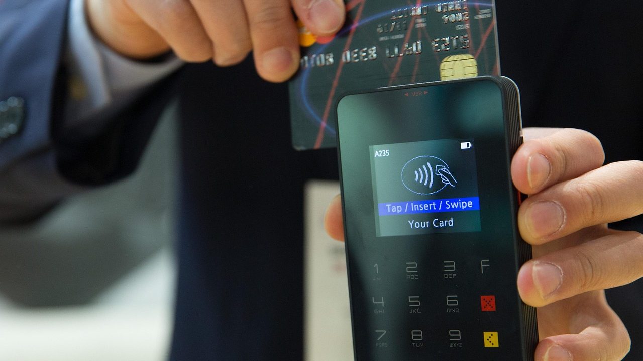 A person holding a smartphone near a contactless payment terminal at a checkout counter.