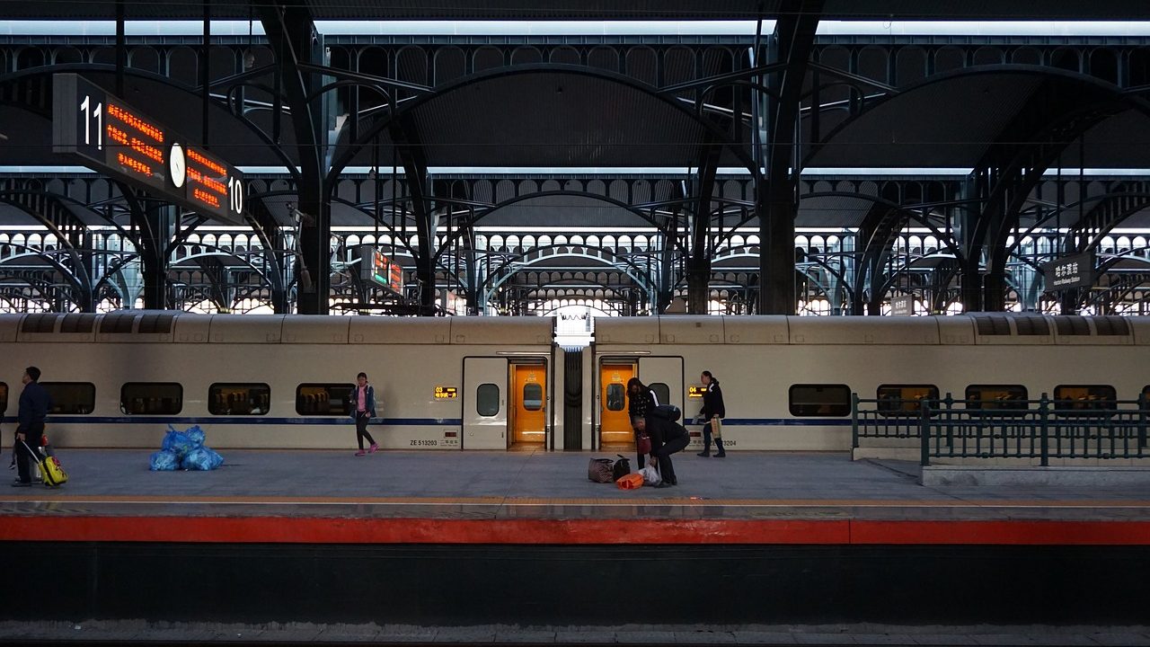 Crowds of commuters moving through a large busy railway station with multiple platforms.