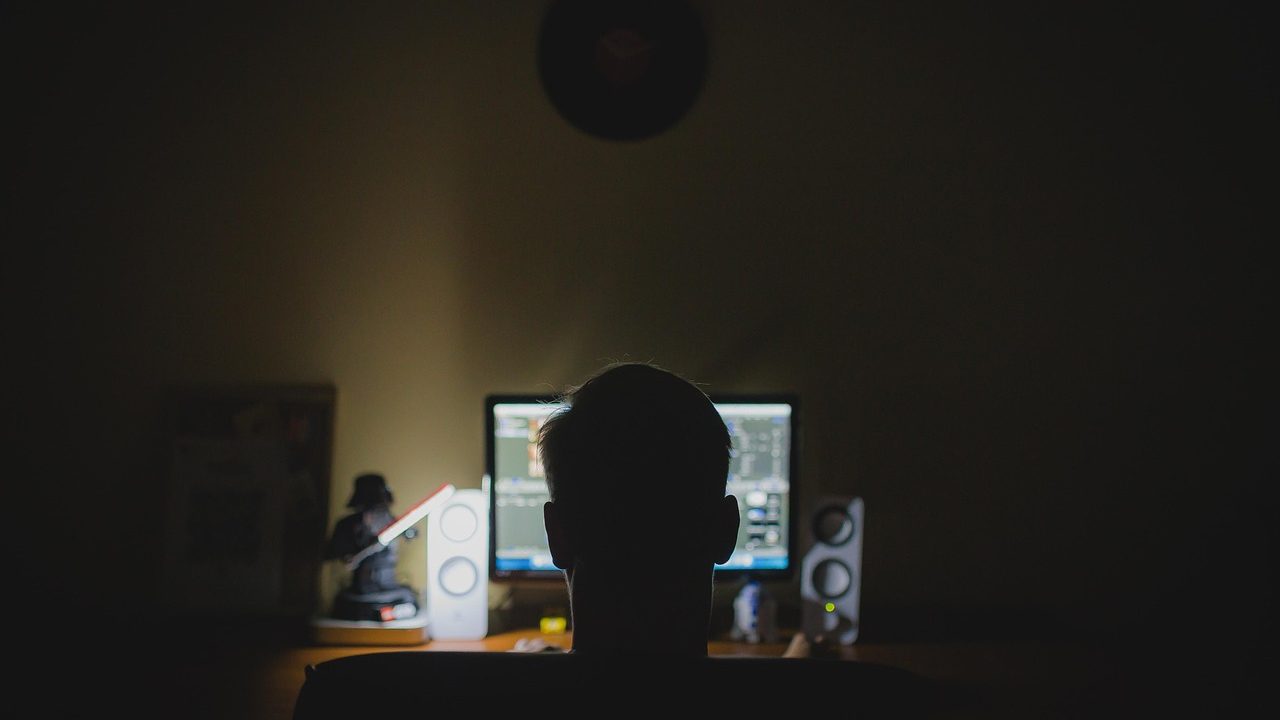 A glowing laptop screen displays lines of code in a dimly lit workspace.