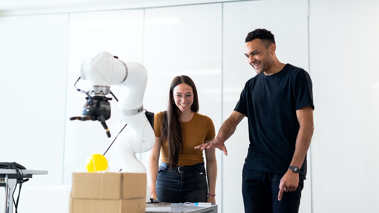 A humanoid robot arm reaching toward an object on a white laboratory table.