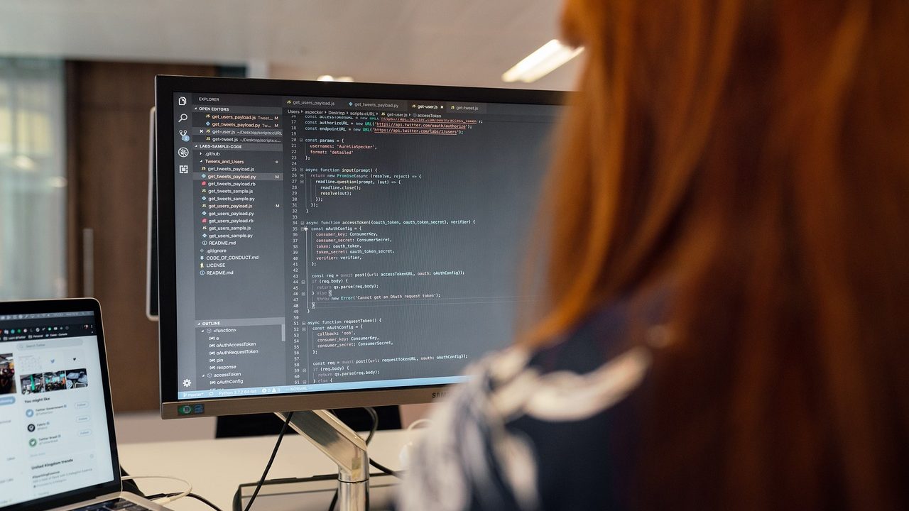 A developer's desk with two monitors displaying lines of code in a dimly lit office.