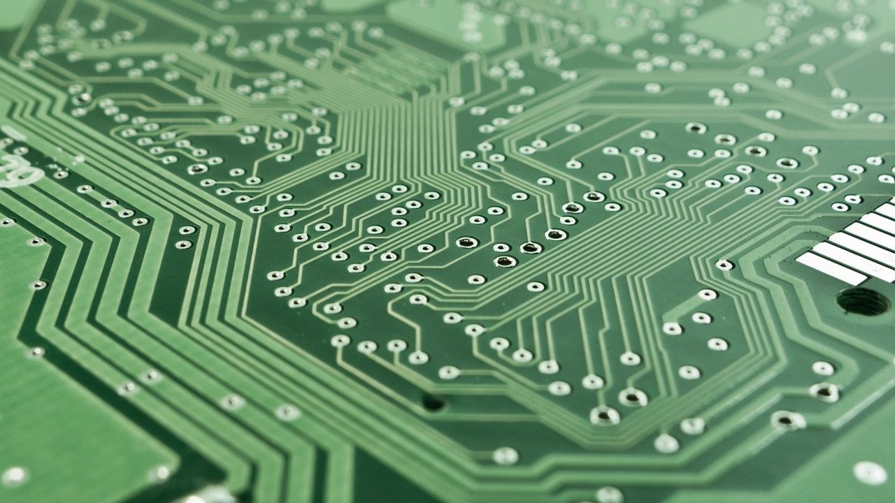 Extreme close-up of a green printed circuit board showing transistors, capacitors, and trace lines.