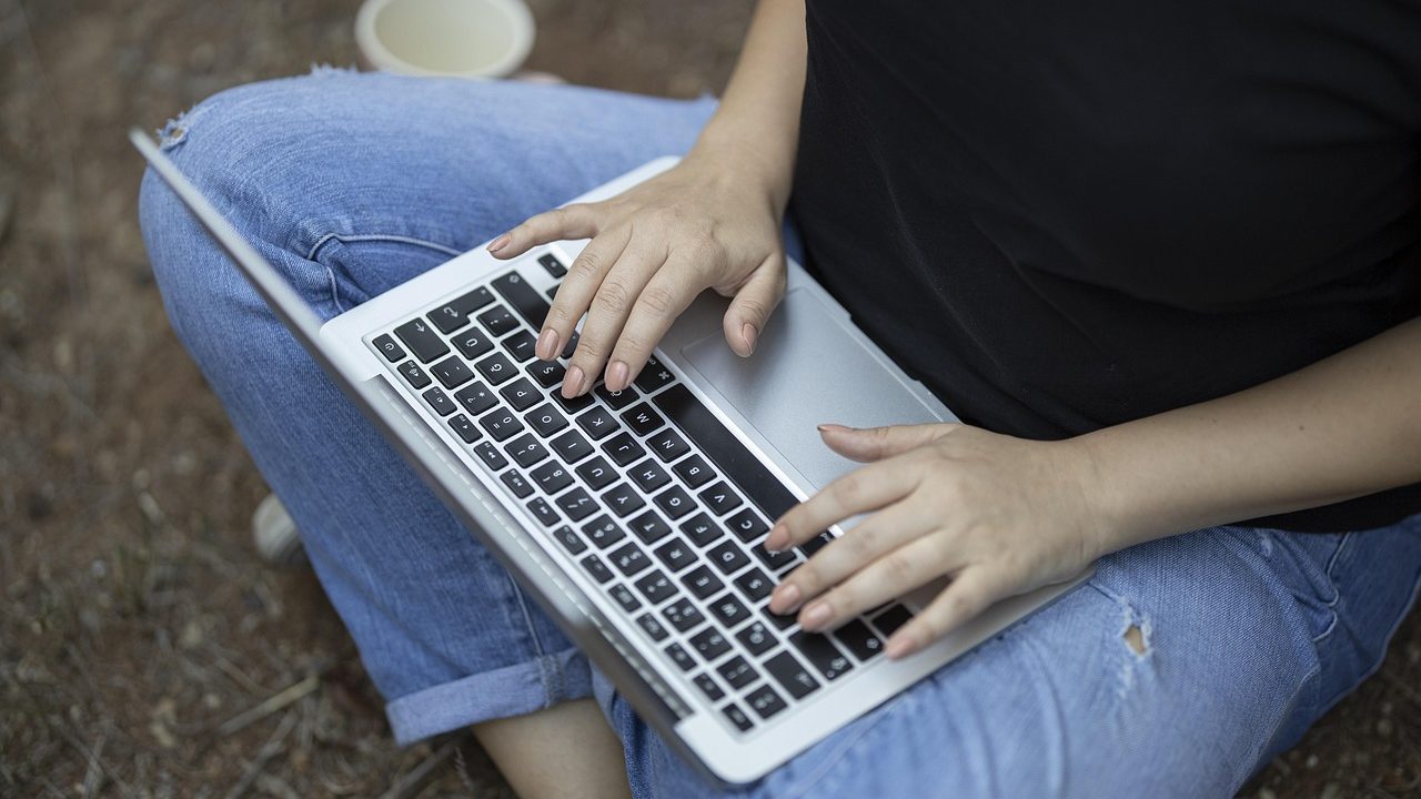 A laptop open on a wooden desk beside a steaming coffee cup in morning light.