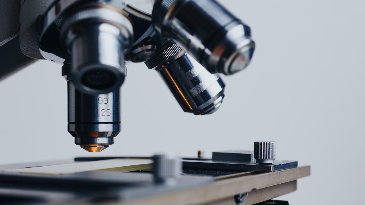 A researcher looks into a microscope in a bright clinical laboratory setting.