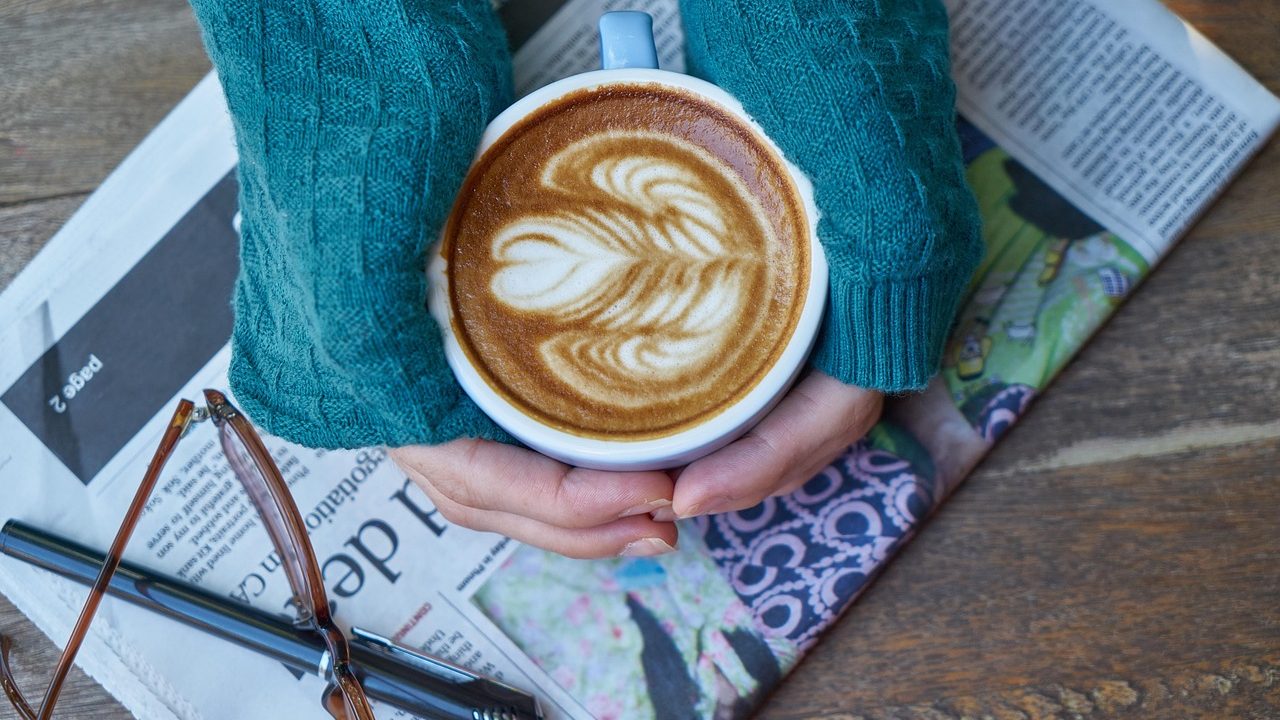 A laptop open to a news feed beside a coffee cup on a wooden desk.