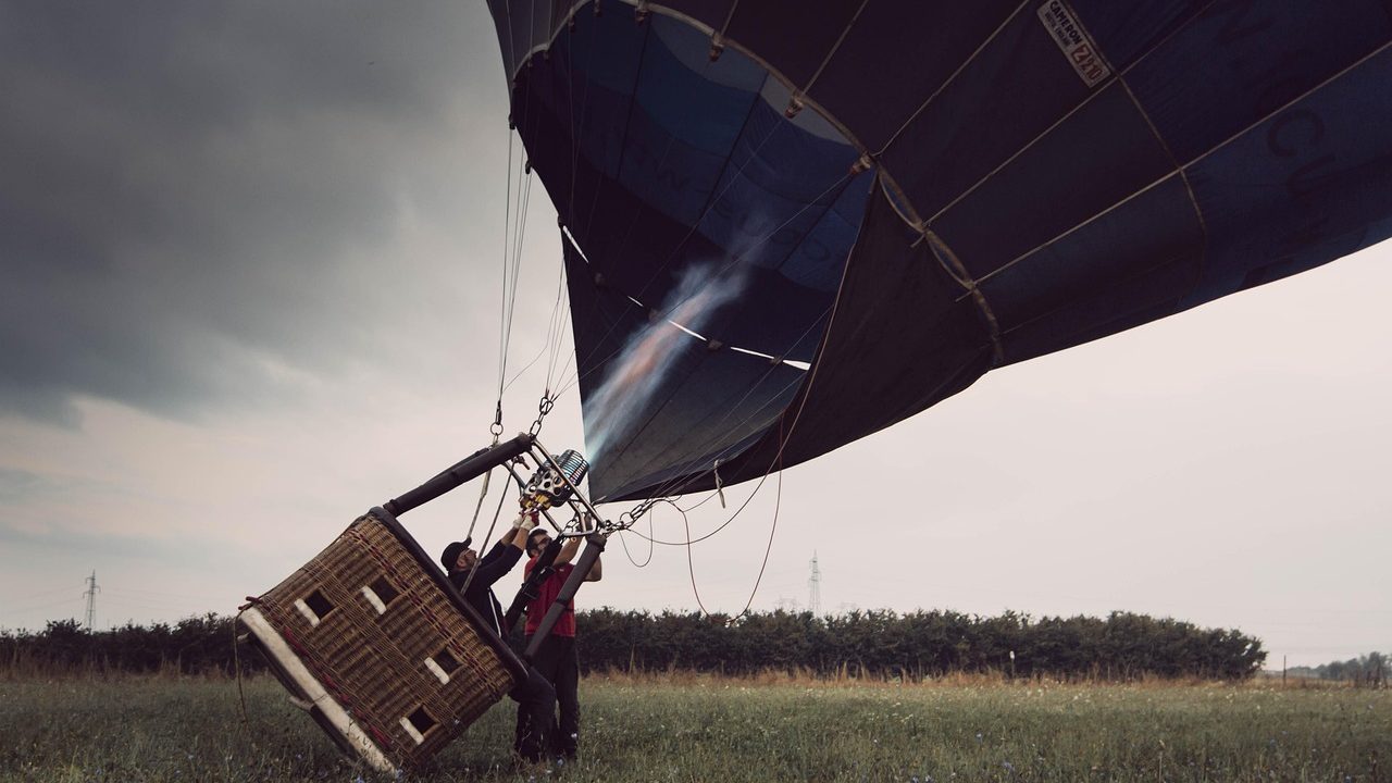 A large white weather balloon being released into a clear blue sky from an open field.