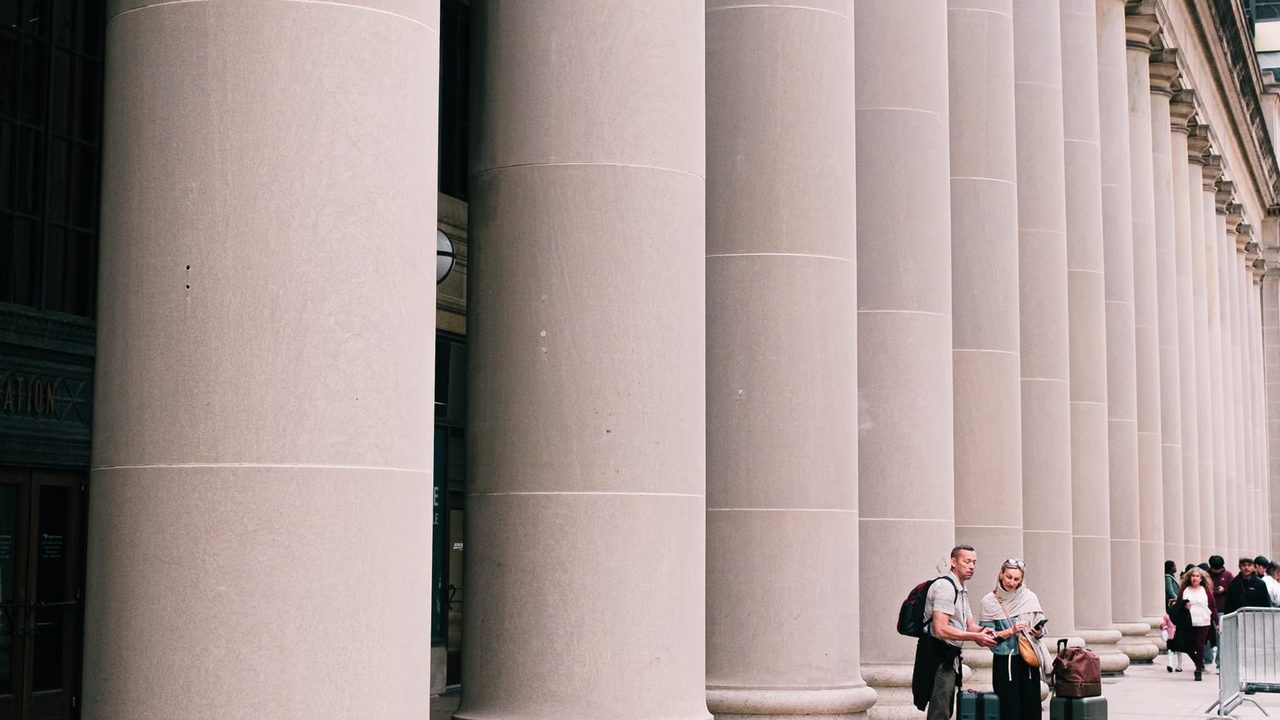 Stone columns rise along the facade of a classical government building under a clear sky.