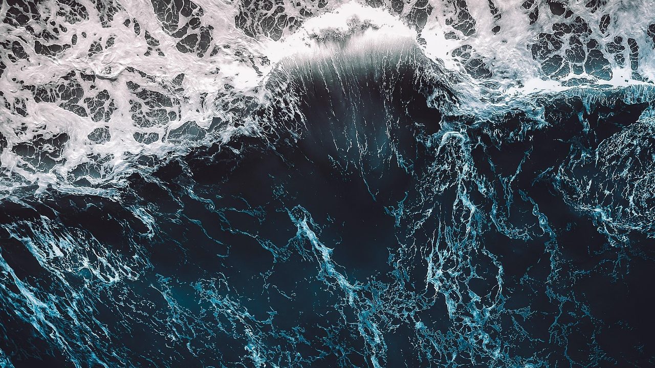 An aerial view of open ocean with sunlight reflecting off deep blue water and white-capped waves.