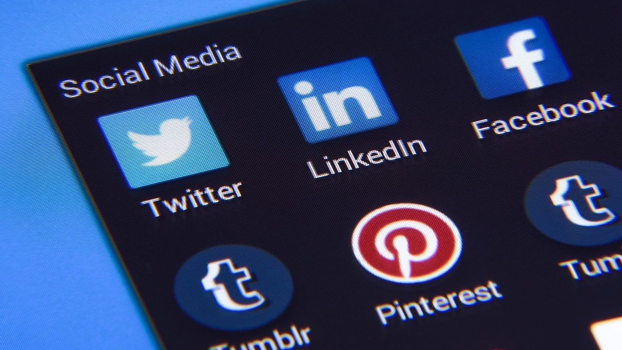 A hand holding a smartphone displaying social media application icons.
