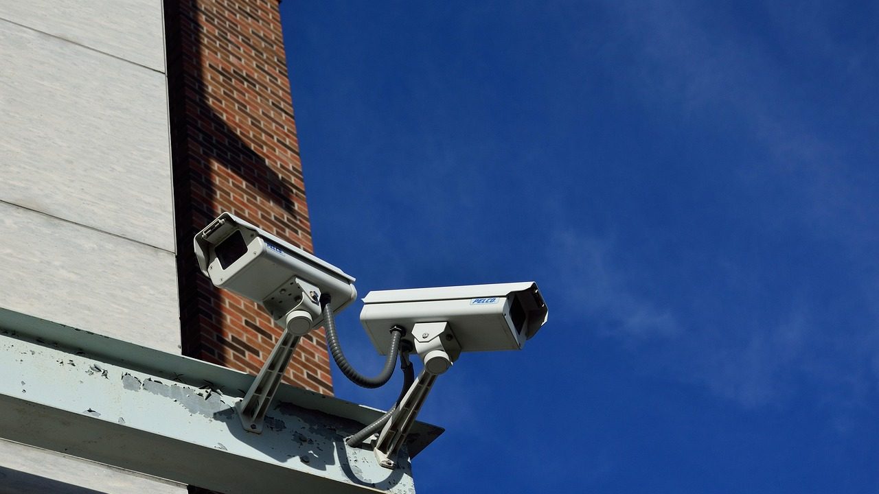 A row of surveillance cameras mounted on a metal pole along an urban street.