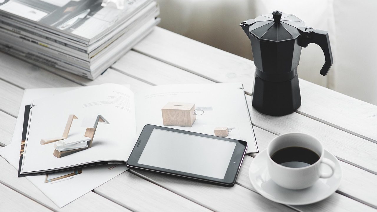A person reads news on a tablet at a café table with a coffee cup nearby.