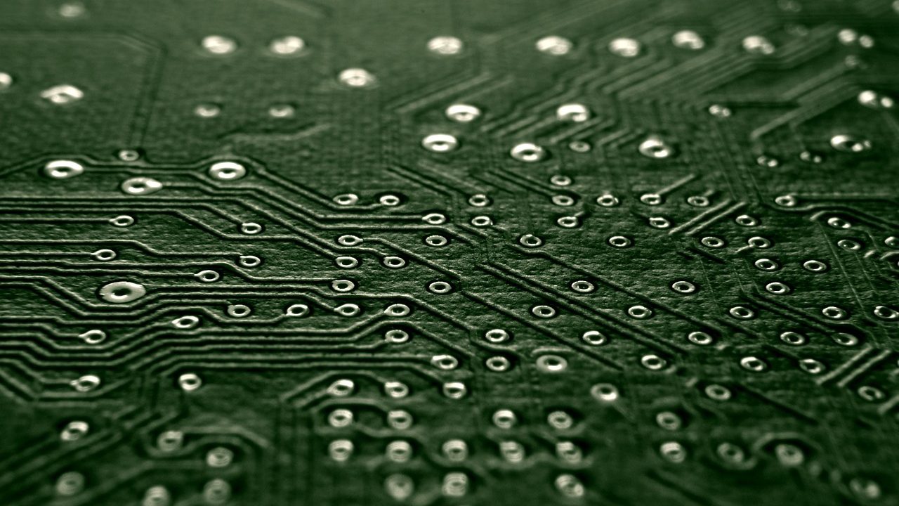 Extreme close-up of a green circuit board with copper traces and microchip components.