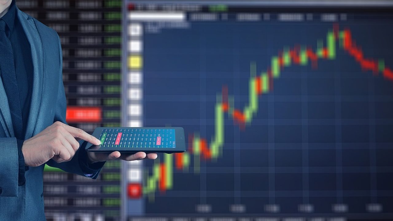 Traders at workstations on a busy stock exchange trading floor surrounded by screens.