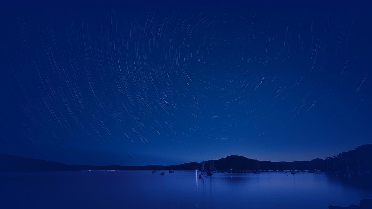 A bright meteor streaks across a dark night sky leaving a glowing trail.