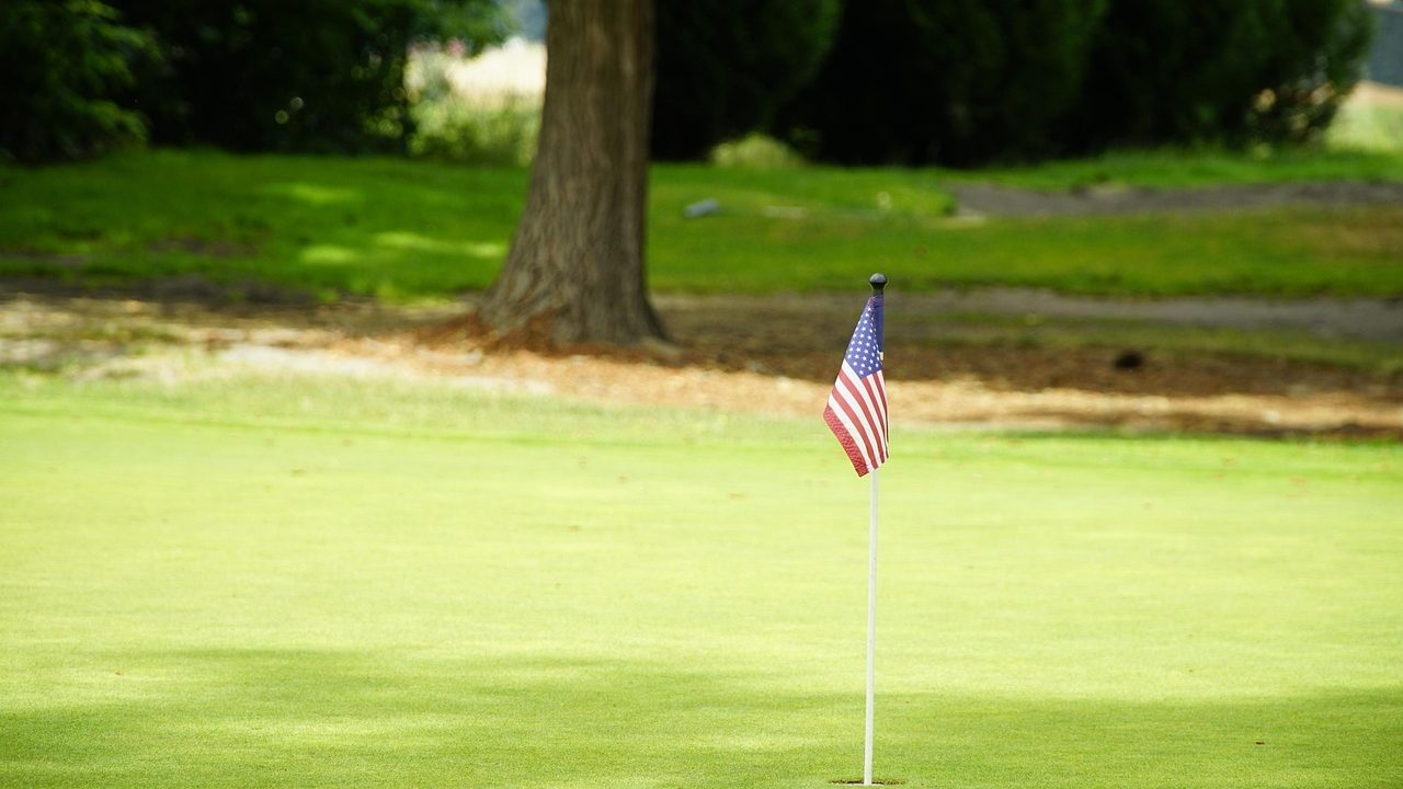 A golf flag stands in a hole on a manicured green with a fairway visible in the background.