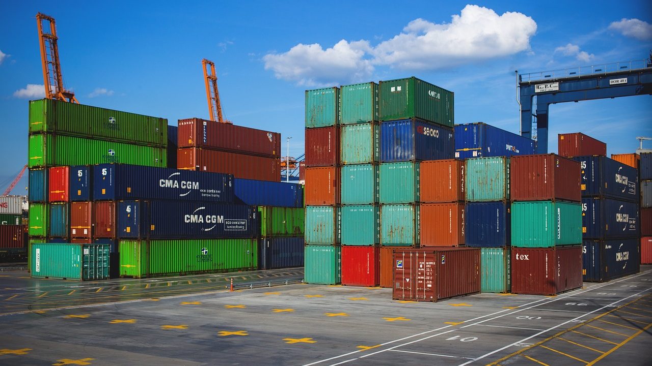A busy commercial seaport with stacked shipping containers and large cranes.