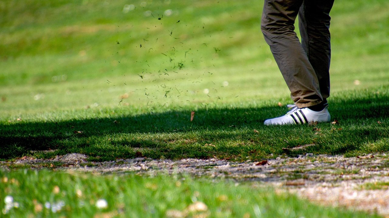 A well-manicured golf course fairway stretches toward a distant green under blue sky.