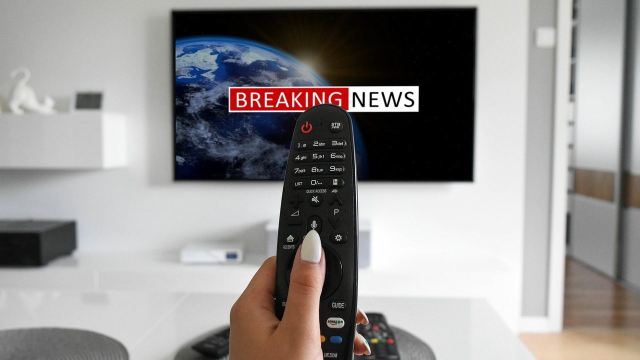 Multiple television screens displaying breaking news broadcasts in a dimly lit studio.