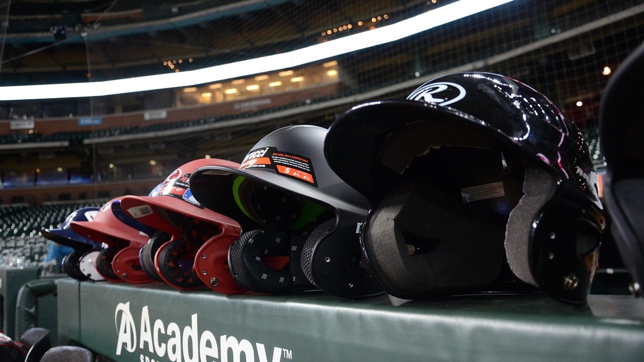 An empty wooden baseball dugout bench with helmets and equipment in the background.