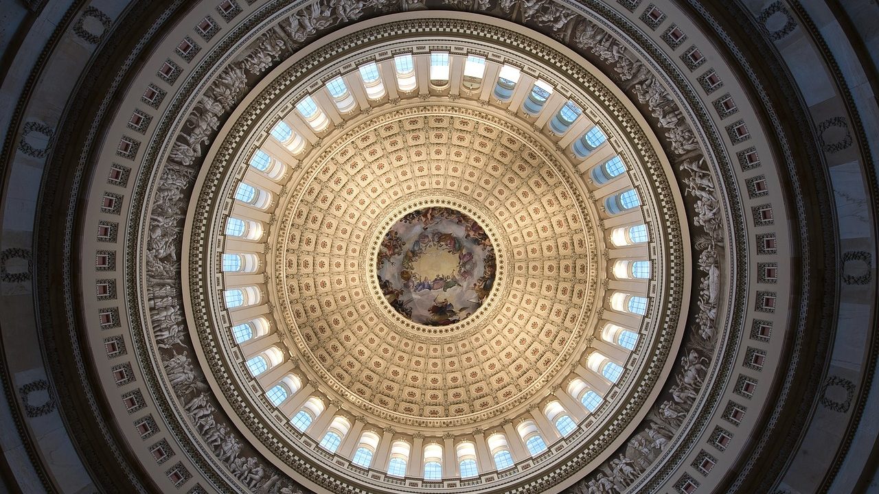The interior of a grand legislative chamber dome with ornate columns and gallery seating.