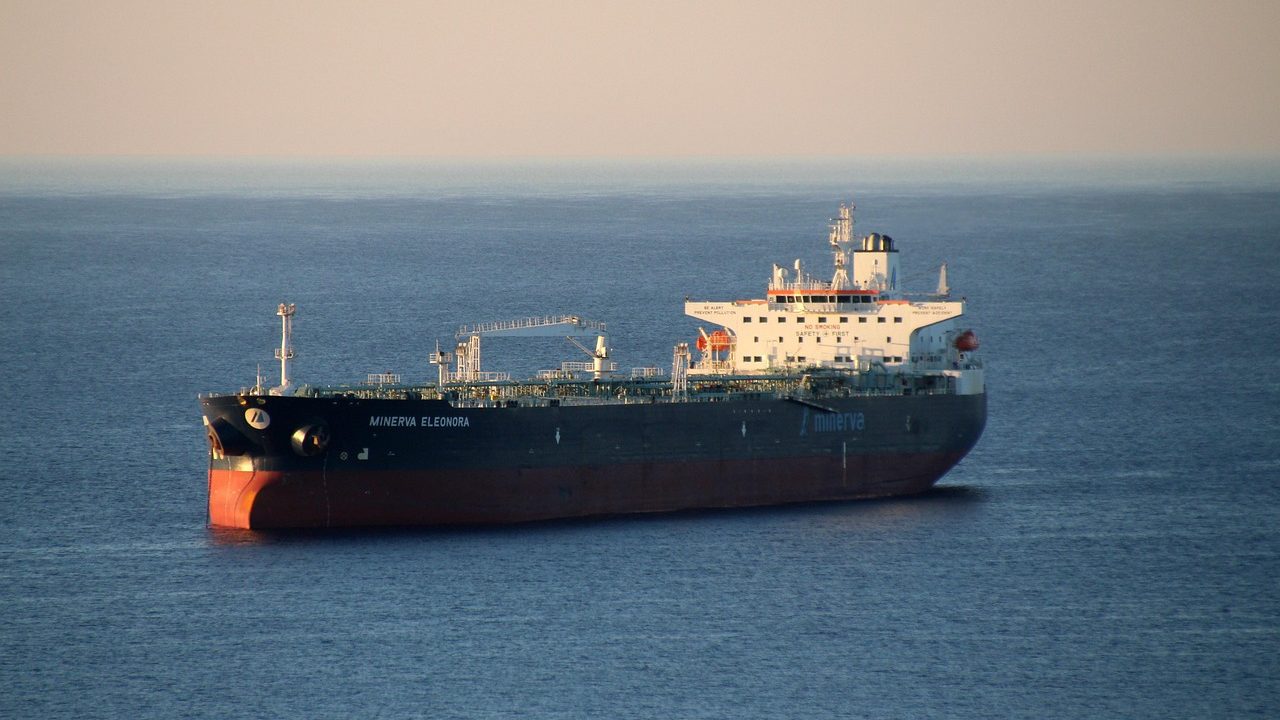 A large oil tanker passes through a narrow strait under a clear sky.