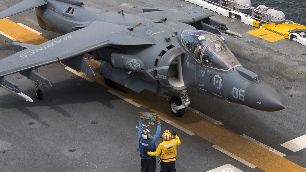 Military aircraft lined up on the deck of a naval aircraft carrier at sea.