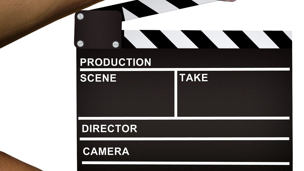 A film clapperboard held open in front of blurred studio lighting equipment.
