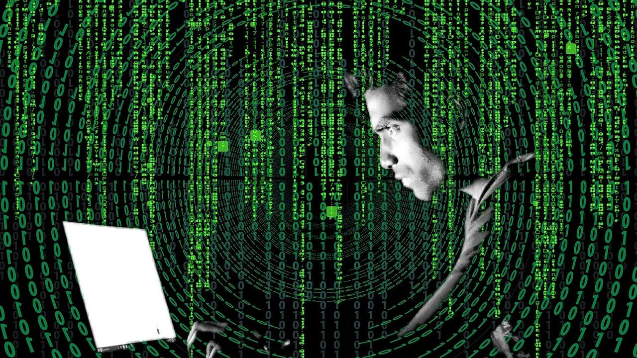 Green lines of code scroll across a dark monitor screen in a dimly lit office.