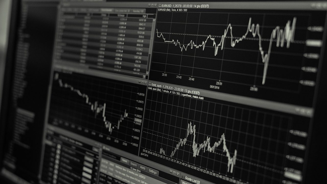 Multiple financial data monitors glow with charts and figures at an empty trading workstation.