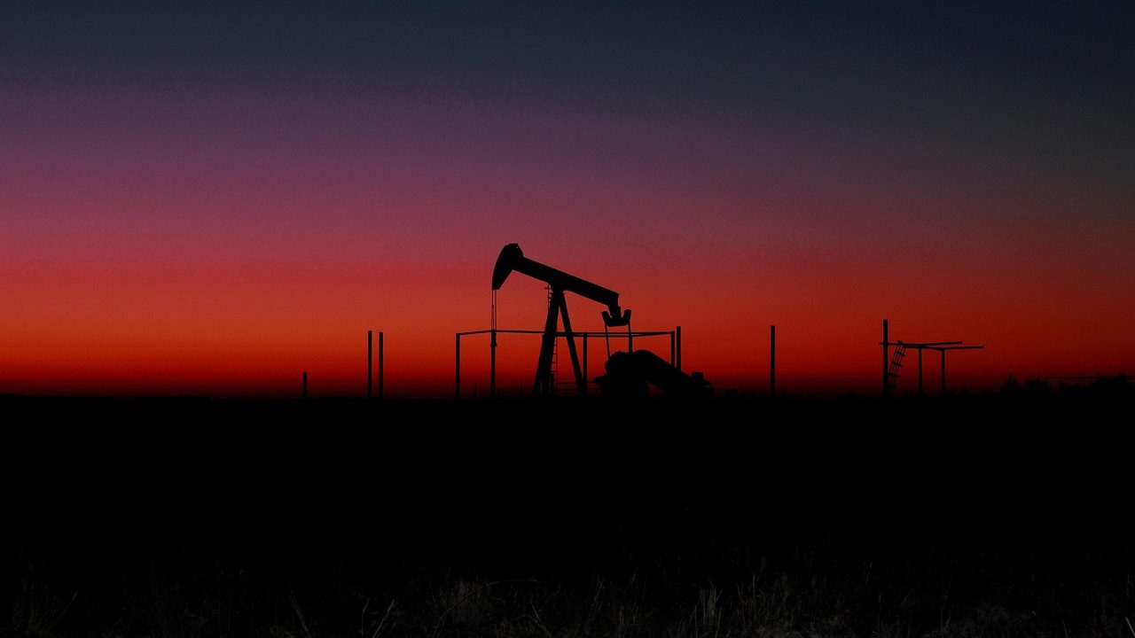 An oil refinery lit up at dusk with flare stacks burning against a darkening sky.