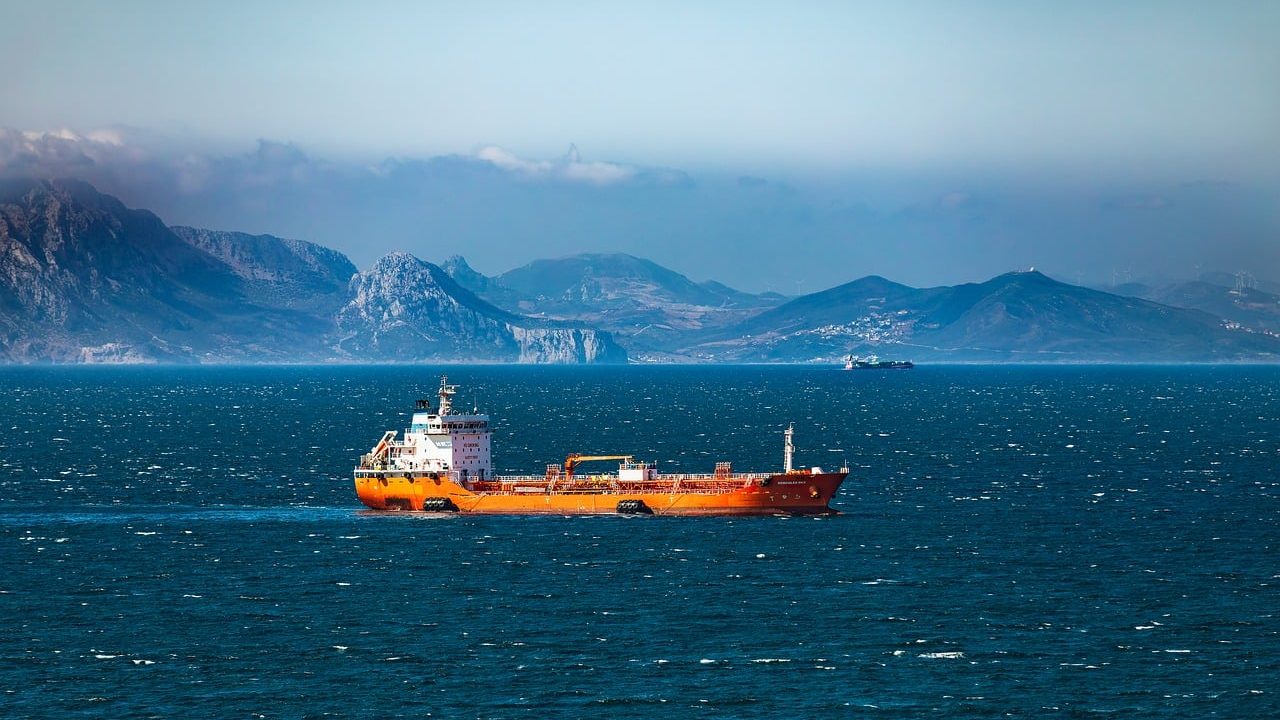 A large oil tanker vessel sailing across open blue ocean water under a clear sky.