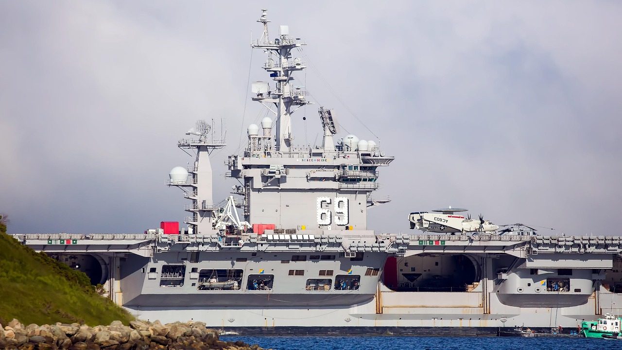 A gray naval warship steams across open blue ocean water under a cloudy sky.