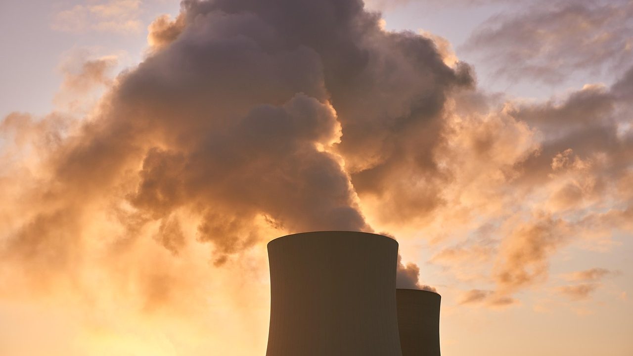 Industrial cooling towers at a large power plant emit steam against a gray sky.