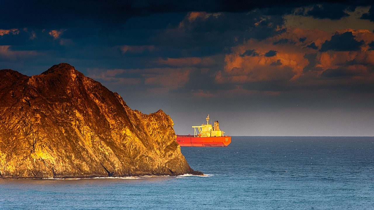 A large oil tanker navigates a narrow strait under overcast skies.