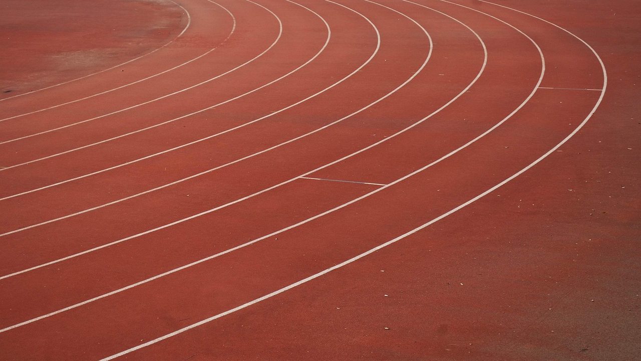 An empty running track inside a large athletics stadium with tiered seating.