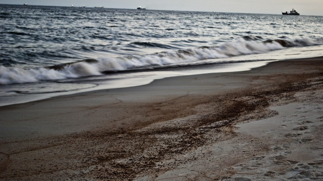 Orange containment booms floating on water to contain an oil spill near a shoreline.