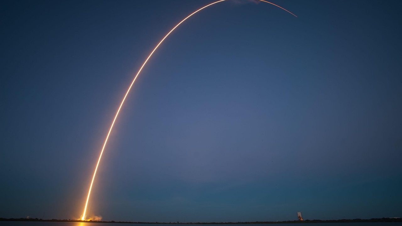 A rocket on a launch pad silhouetted against a bright sky at dusk.