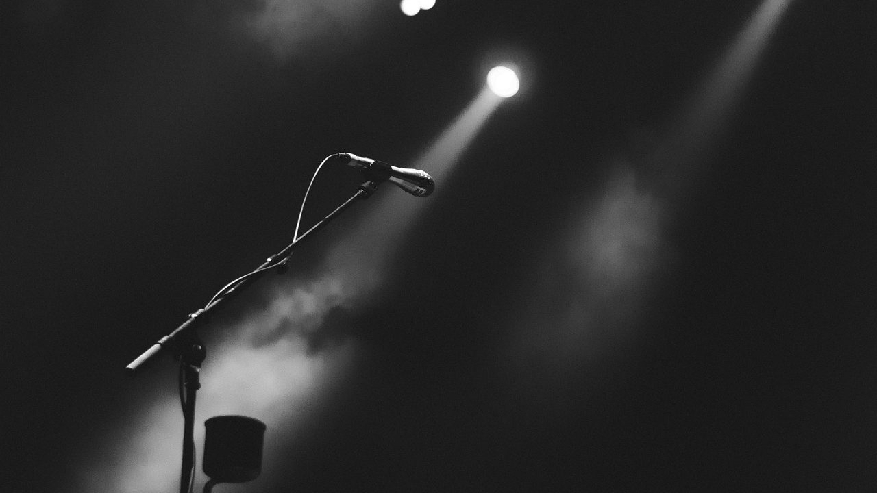 An empty concert stage lit by a single dramatic spotlight in a darkened arena.