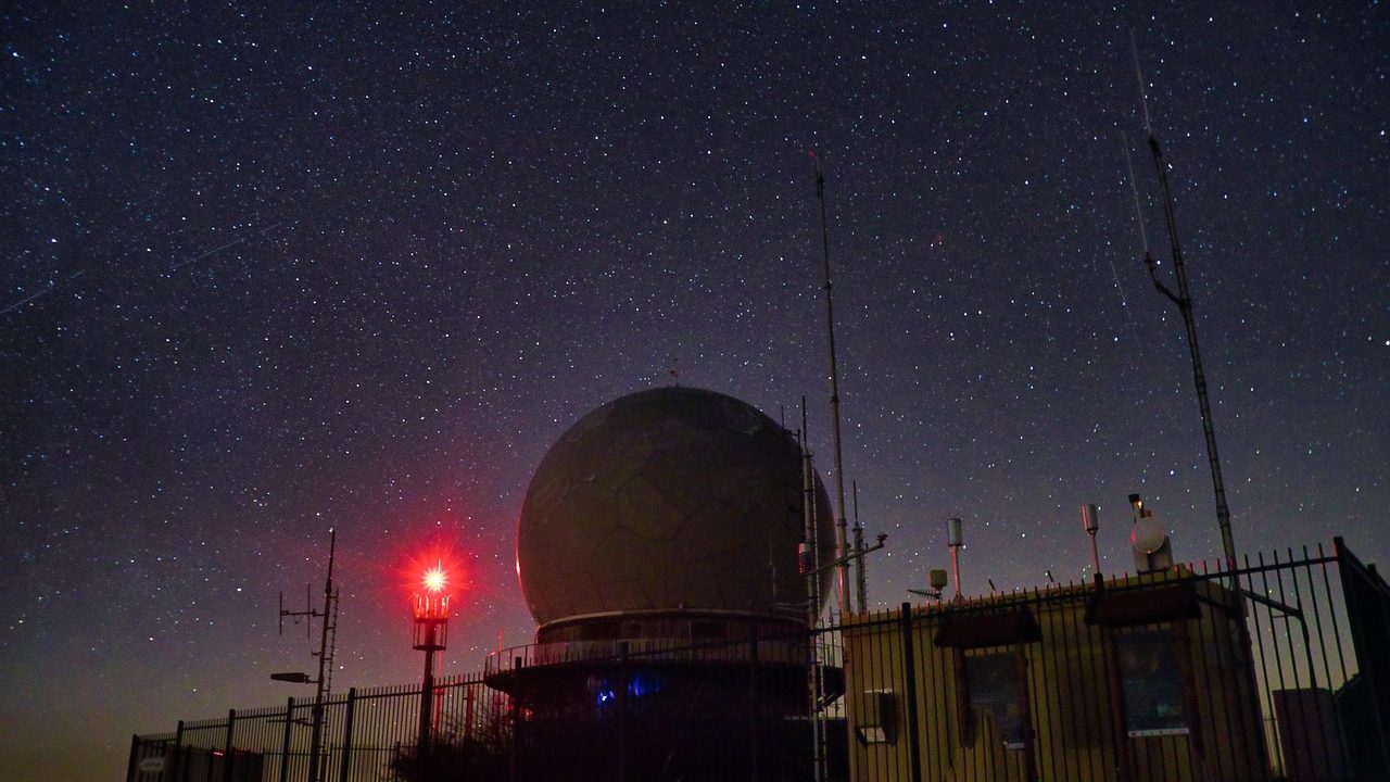 A large observatory dome open to a star-filled night sky on a dark hilltop.