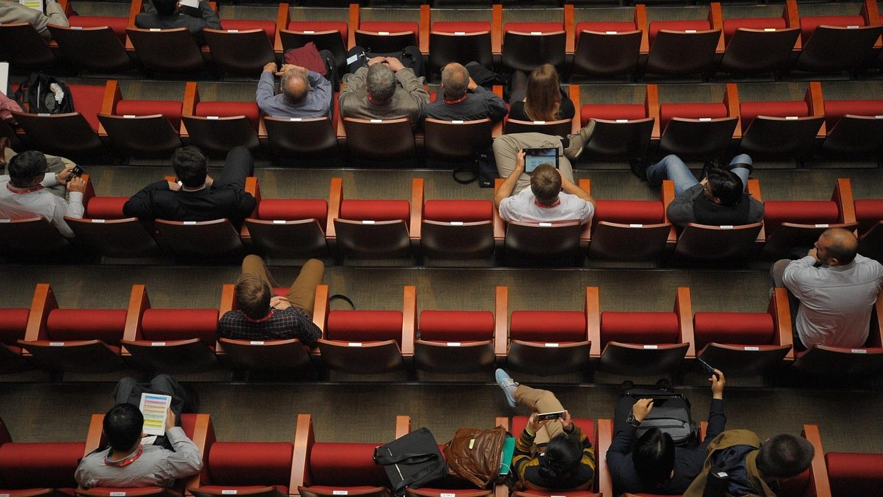 A speaker's podium with a microphone stands before rows of empty delegate chairs in a conference hall.