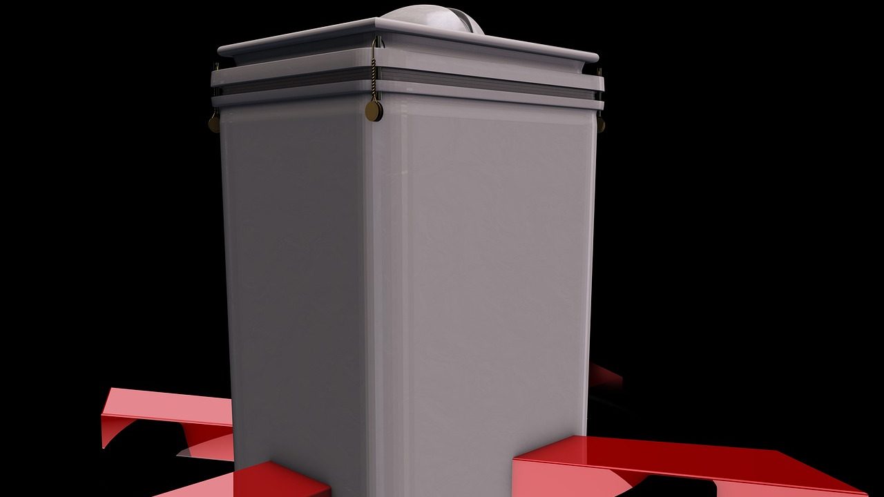 A sealed wooden ballot box with a narrow slot on top sits on a table in a formal chamber.
