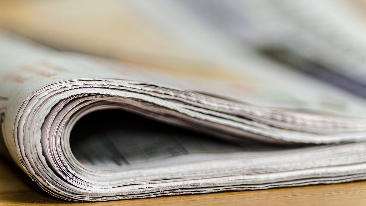 Large rolls of paper feed through an industrial printing press in a production facility.