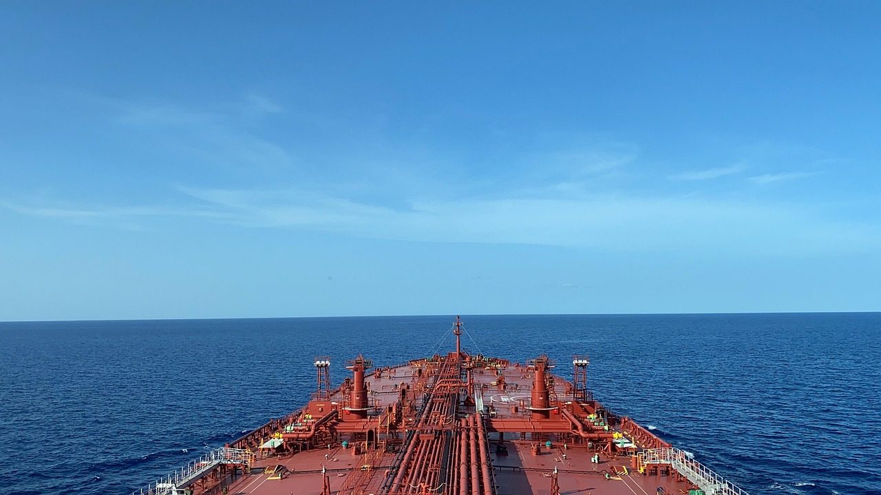 A large cargo ship steams across open ocean under a cloudy sky.