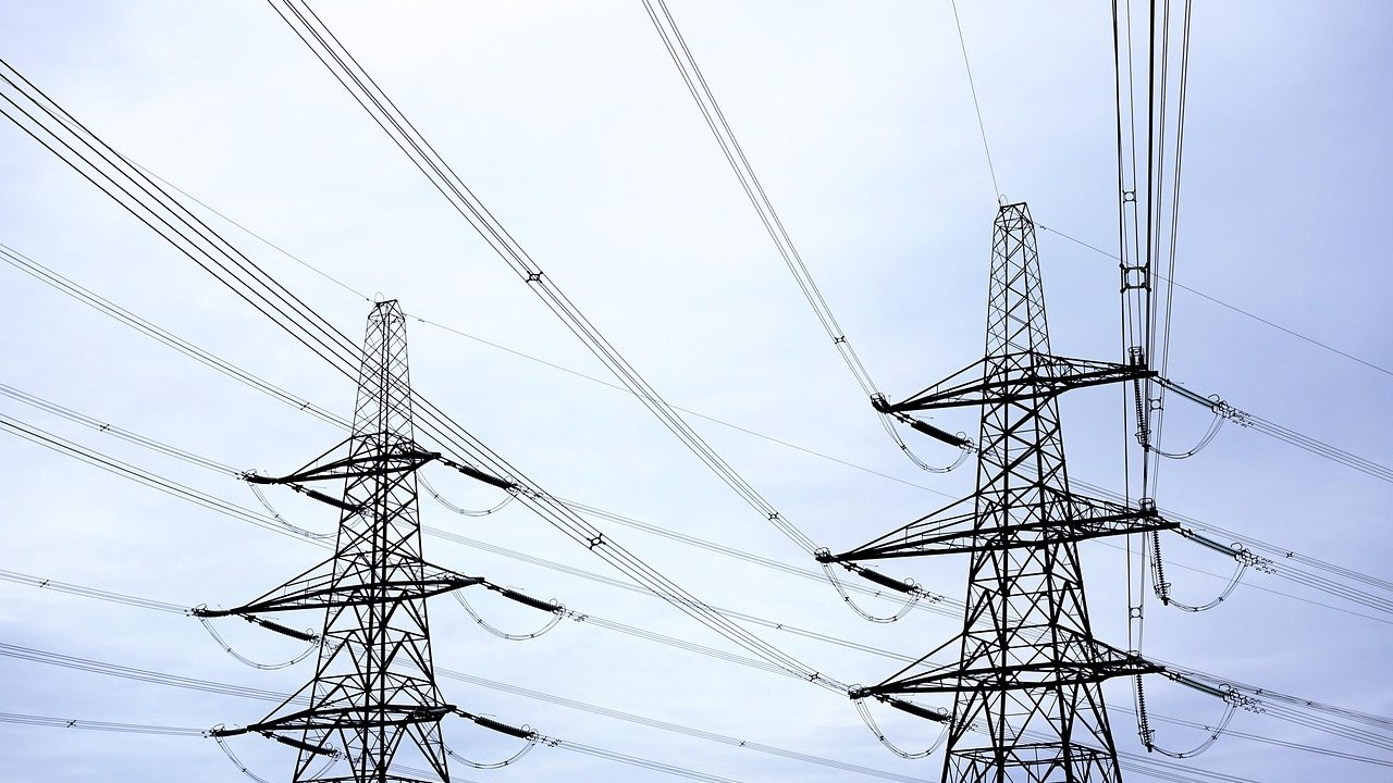 High-voltage transmission towers and power lines stretch across a flat landscape at dusk.