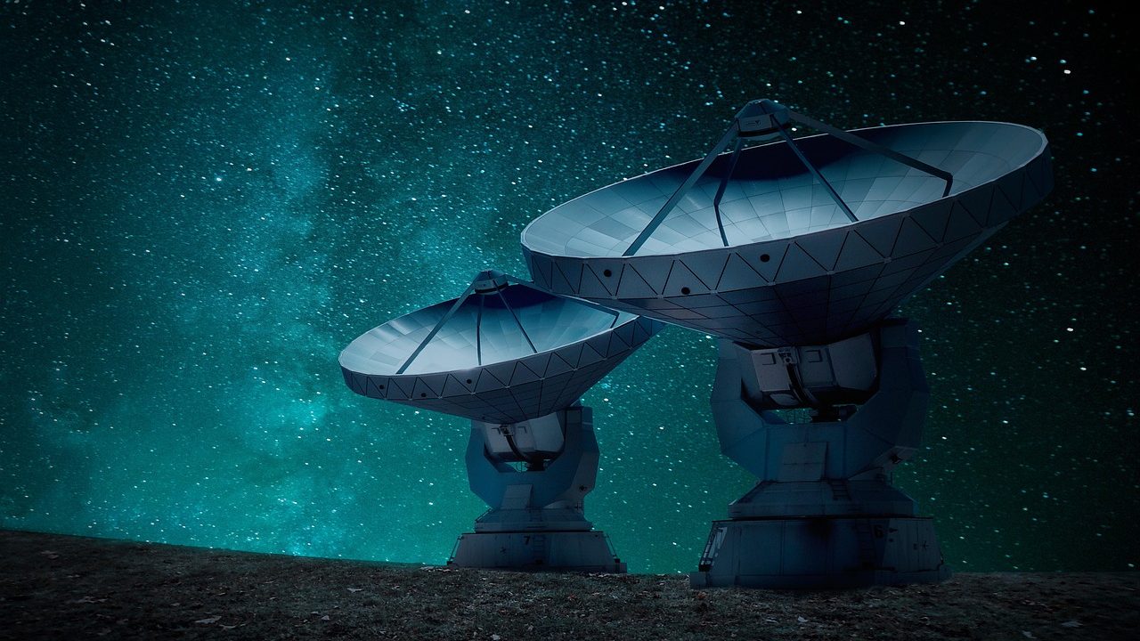 A cluster of large white satellite communication dishes pointed skyward against a clear blue sky.