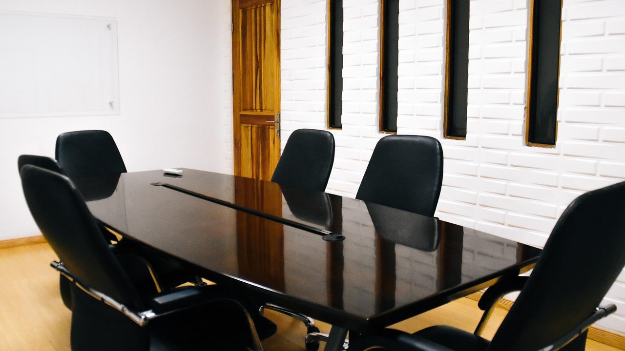 A long polished conference table with empty chairs in a modern corporate boardroom.