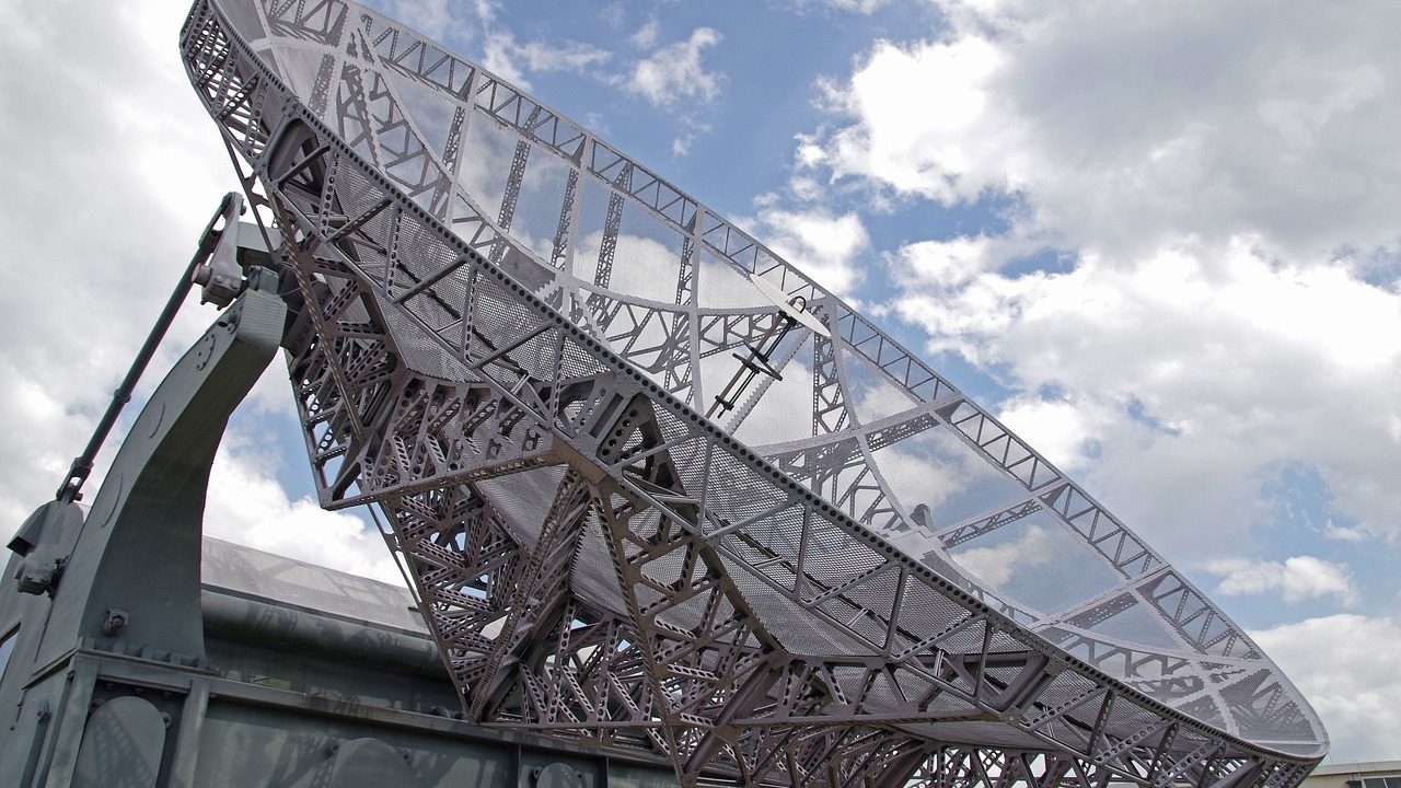 A large rotating radar dish antenna mounted on a steel tower against an open sky.